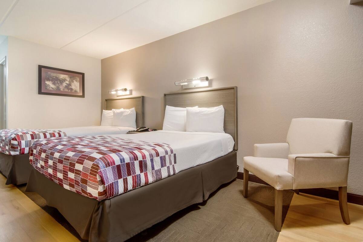 A hotel room with two beds, a chair, and a nightstand.