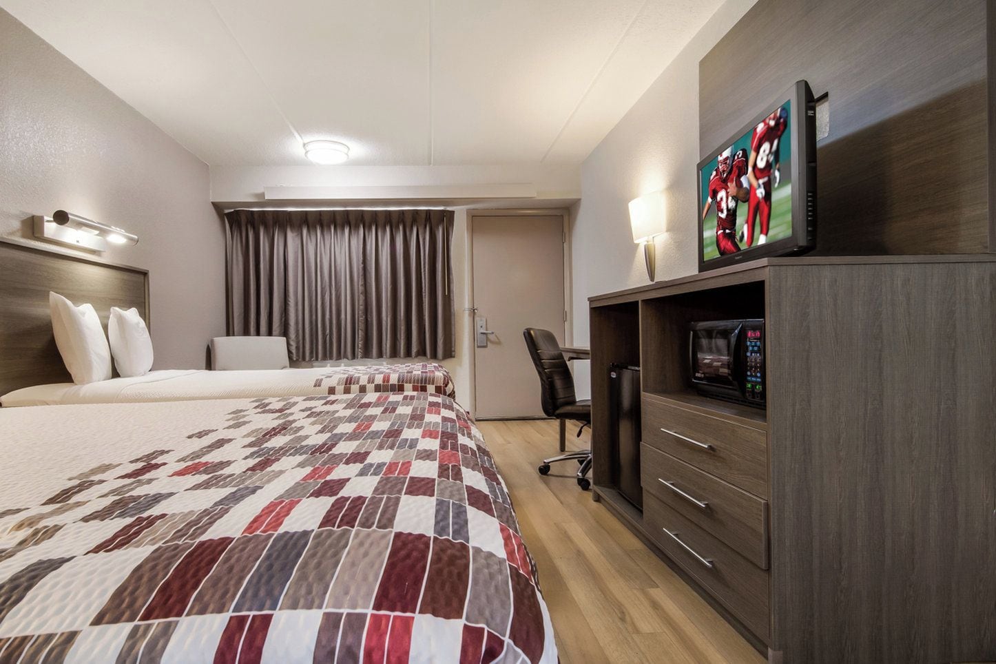 Une chambre d’hôtel avec deux lits, une télévision, un bureau et une chaise.