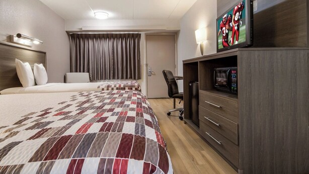 A hotel room with two beds, a TV, a desk, and a chair.