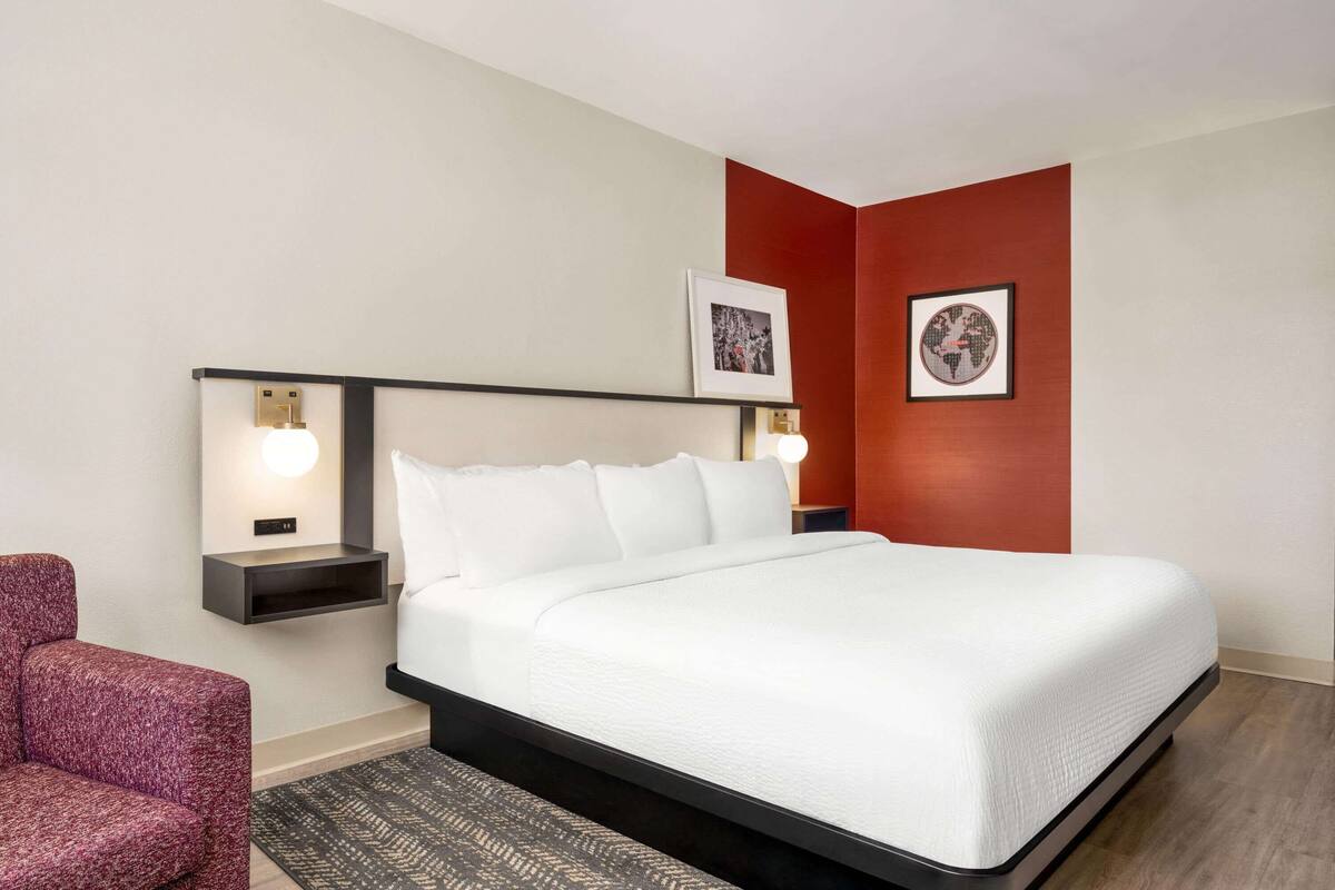 Een keurig opgemaakt hotelkamer met een groot bed, twee nachtkastjes, een rode accentmuur en twee ingelijste foto's.