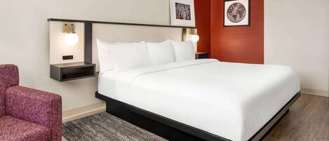 A neatly arranged hotel room with a large bed, two bedside tables, a red accent wall, and two framed pictures.