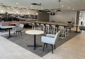 Un café moderno con mesas redondas, taburetes de bar, un mural en la pared y una zona de mostrador.