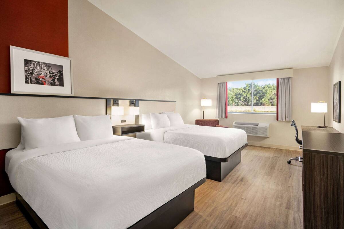 Hotelkamer met twee bedden, een bureau, een stoel, een raam met gordijnen en een ingelijst schilderij aan de muur.