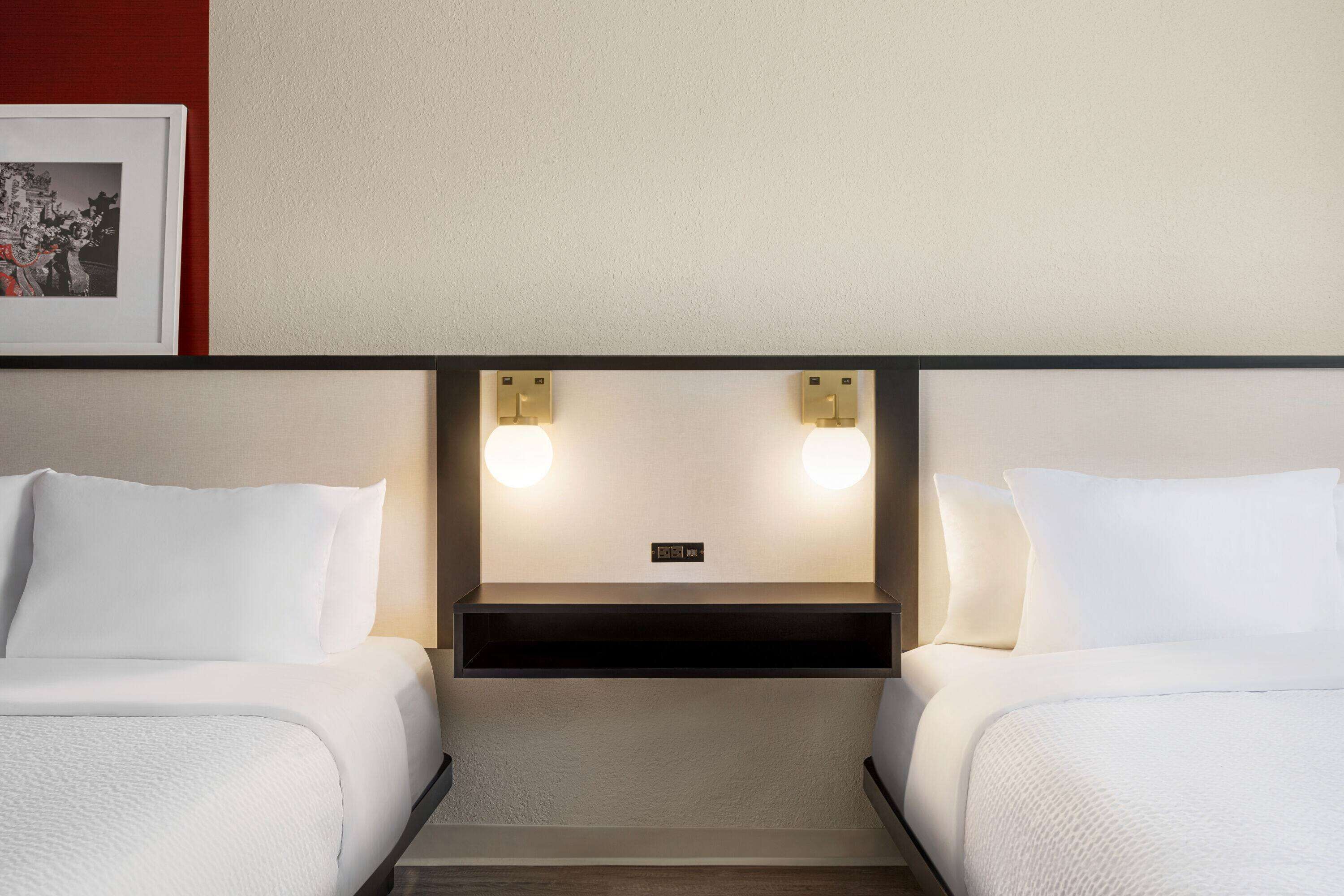 A hotel room with two beds, a headboard with integrated lighting, and a framed picture on the wall.