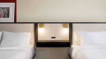 Quarto de hotel com duas camas, cabeceira com iluminação integrada e um quadro pendurado na parede.