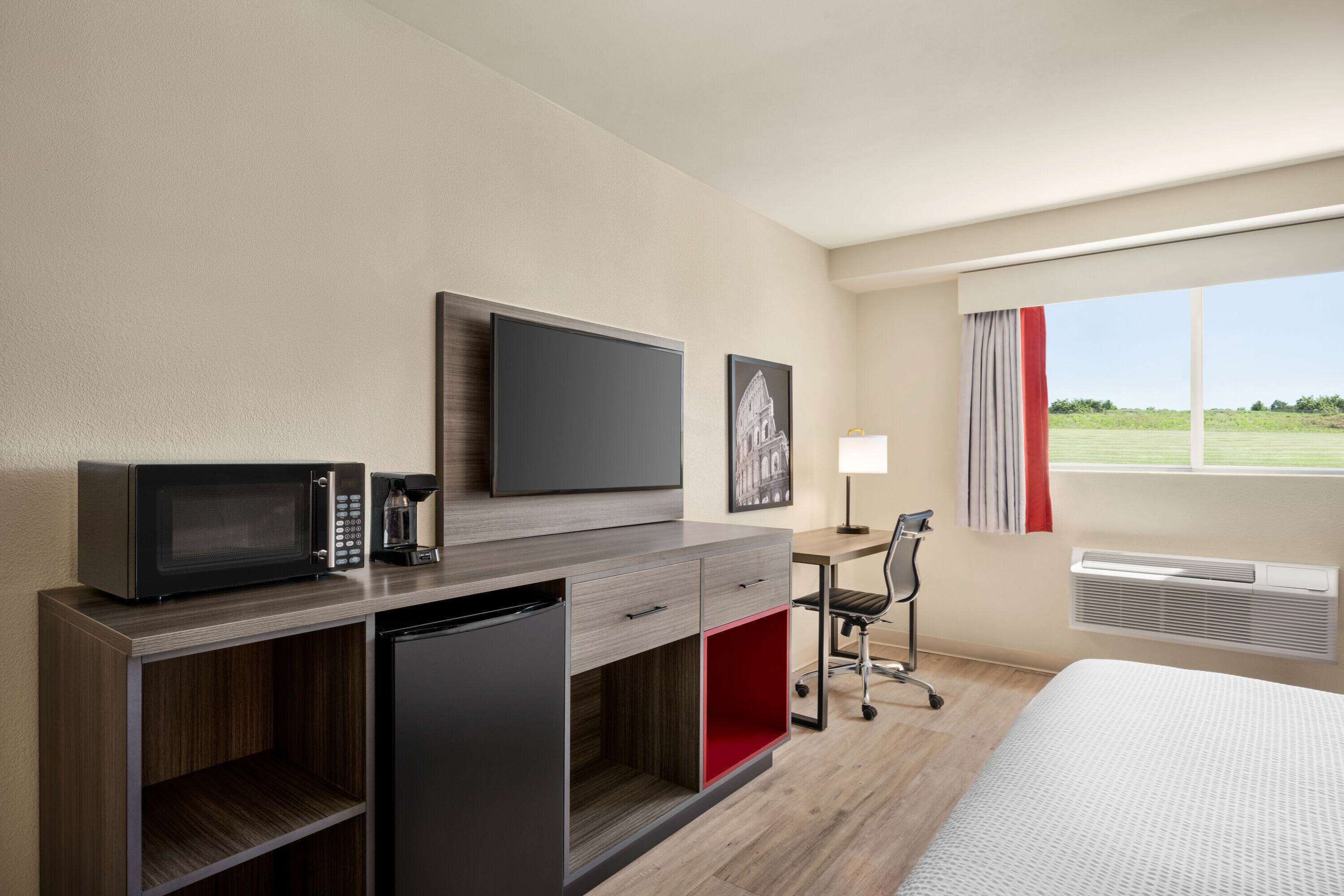 Une chambre d’hôtel équipée d’un lit, d’un bureau avec une chaise, d’un four à micro-ondes, d’une machine à café et d’une télévision.