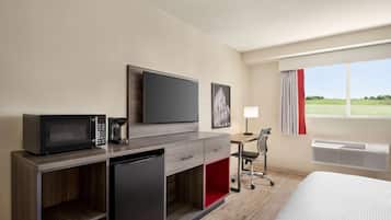 Quarto de hotel com cama, escrivaninha com cadeira, micro-ondas, cafeteira e televisão.