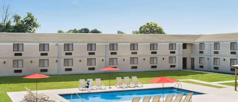 A hotel with a swimming pool, outdoor seating, and a covered area with umbrellas.