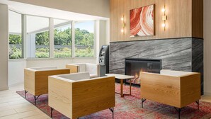 A modern living room with a fireplace, wooden furniture, and a large window offering a view of greenery. - Ramada by Wyndham Allentown/Bethlehem (Whitehall)
