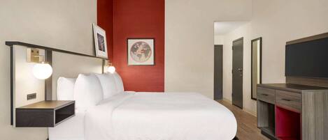 A hotel room with a bed, bedside tables, a TV, and a red accent wall.