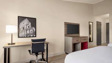 Habitación de hotel con cama, escritorio, silla, televisión, armario y un cuadro con la imagen del Coliseo.