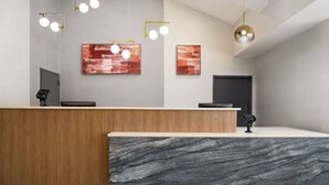 A reception desk with a marble front, wooden paneling, and modern lighting fixtures. - Ramada by Wyndham Allentown/Bethlehem (Whitehall)