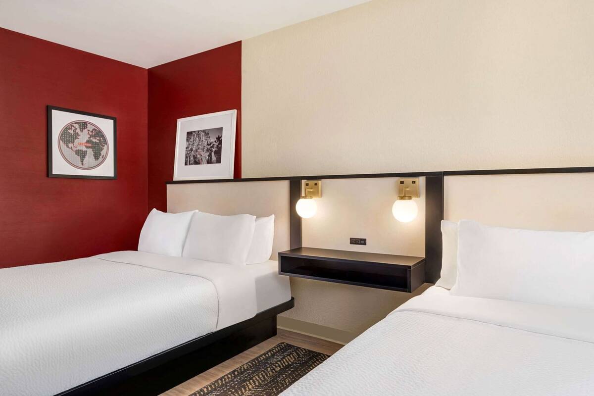 Een hotelkamer met twee bedden, een rode wand en twee ingelijste foto's.