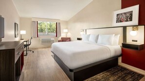 A hotel room with a large bed, a desk, a chair, a TV, and a window with curtains. - Ramada by Wyndham Allentown/Bethlehem (Whitehall)