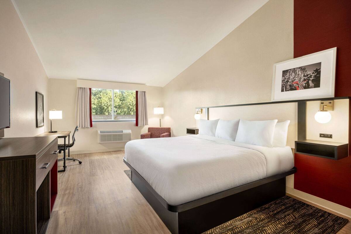 Een hotelkamer met een groot bed, een bureau, een stoel, een televisie en een raam met gordijnen.