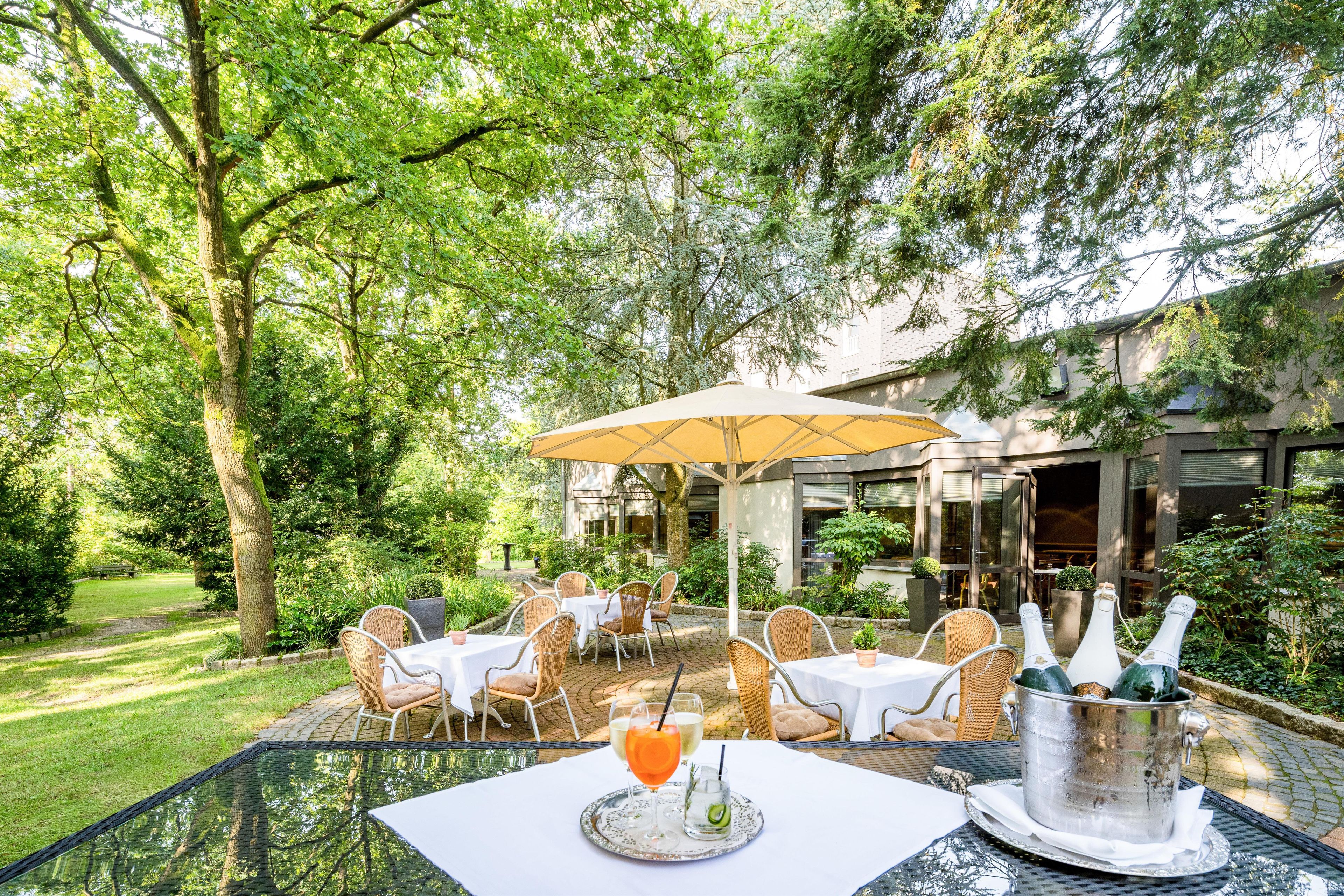 Un área de comedor al aire libre con mesas y sillas, rodeada de exuberante follaje y árboles.