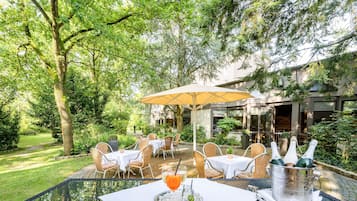 Un área de comedor al aire libre con mesas y sillas, rodeada de exuberante follaje y árboles.