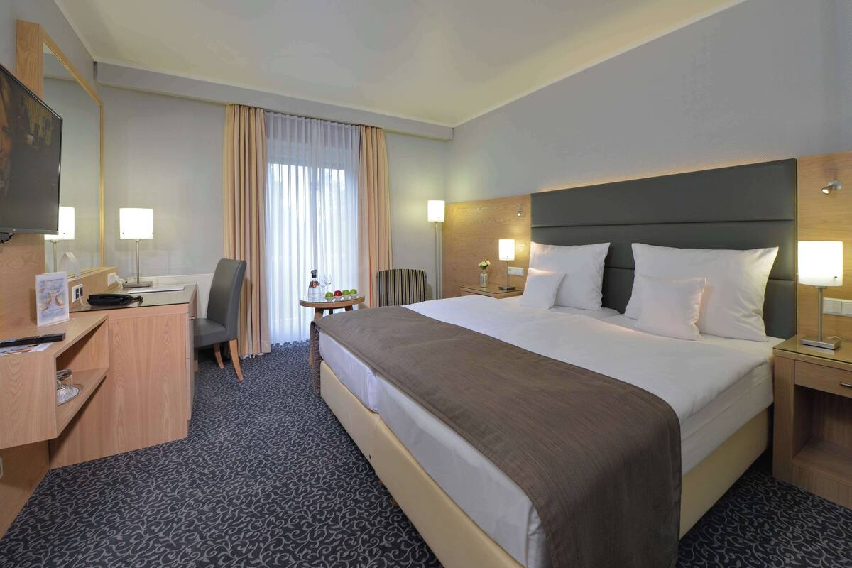 Une chambre d’hôtel avec un grand lit, un bureau avec une chaise, une télévision et une petite table avec une lampe.