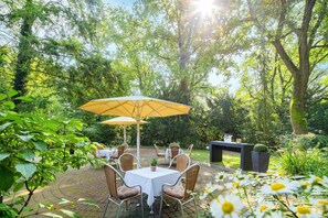 Eine Terrasse im Freien mit Tisch und Stühlen, umgeben von üppiger Bepflanzung und Bäumen.