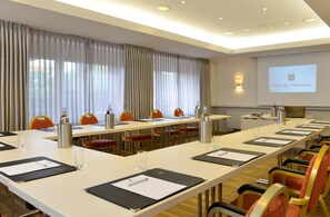 Une salle de conférence avec une longue table, des chaises et un écran de projection sur lequel est affiché le nom « Hotel Der Fohrenhof ».