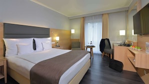 A hotel room with a large bed, a desk, a chair, a TV, and a small table with a lamp. - Best Western Hotel Der Foehrenhof (Hannover)