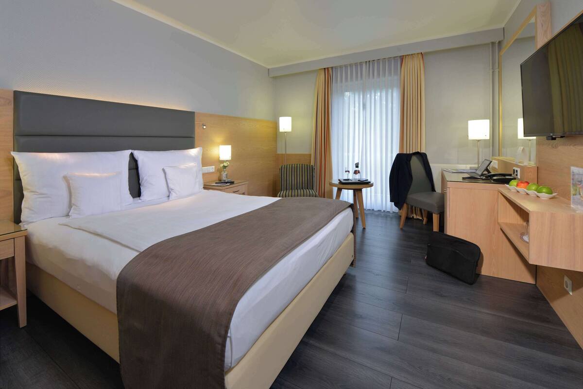 Une chambre d’hôtel avec un grand lit, un bureau, une chaise, une télévision et une petite table avec une lampe.