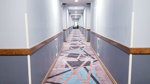 Een lange, smalle hotelgang met een patroon vloerkleed, houten sierlijsten en een plafondlamp.