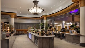 A modern hotel lobby with a central bar area, seating, and a large chandelier. - Hilton Paris Charles de Gaulle Airport (Tremblay-en-France)