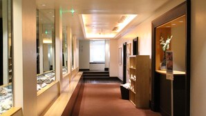 A hotel corridor with a carpeted floor, glass display cases, and a wooden reception desk. - Hilton Paris Charles de Gaulle Airport (Tremblay-en-France)