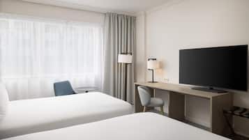 Ein Hotelzimmer mit zwei Betten, einem Schreibtisch, einem Fernseher, einem Sessel und einer Lampe.