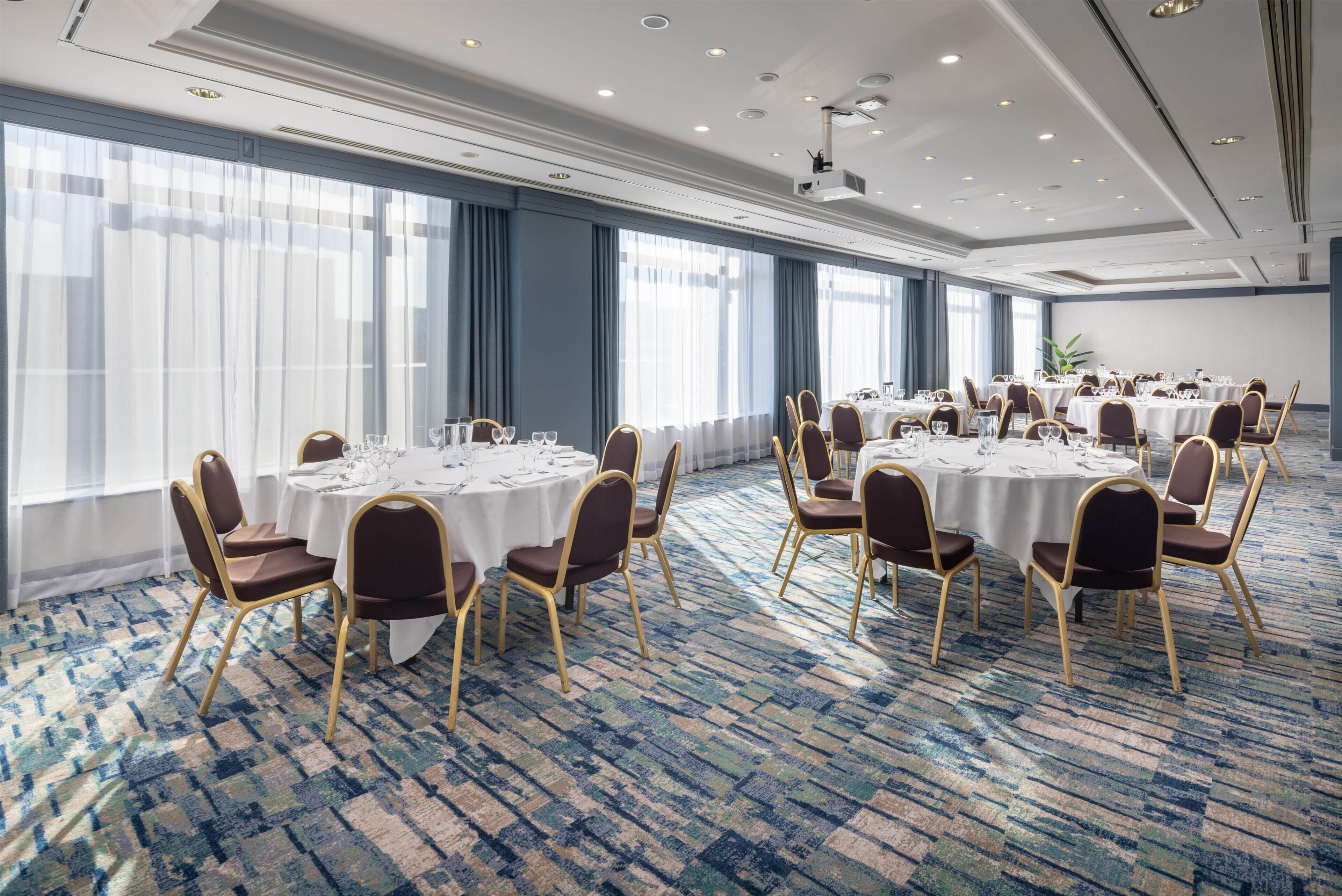 A conference room with round tables, chairs, and a carpeted floor.