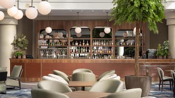 Zona de bar con varias estanterías llenas de botellas, una barra de madera y un área de asientos con mesas y sillas.