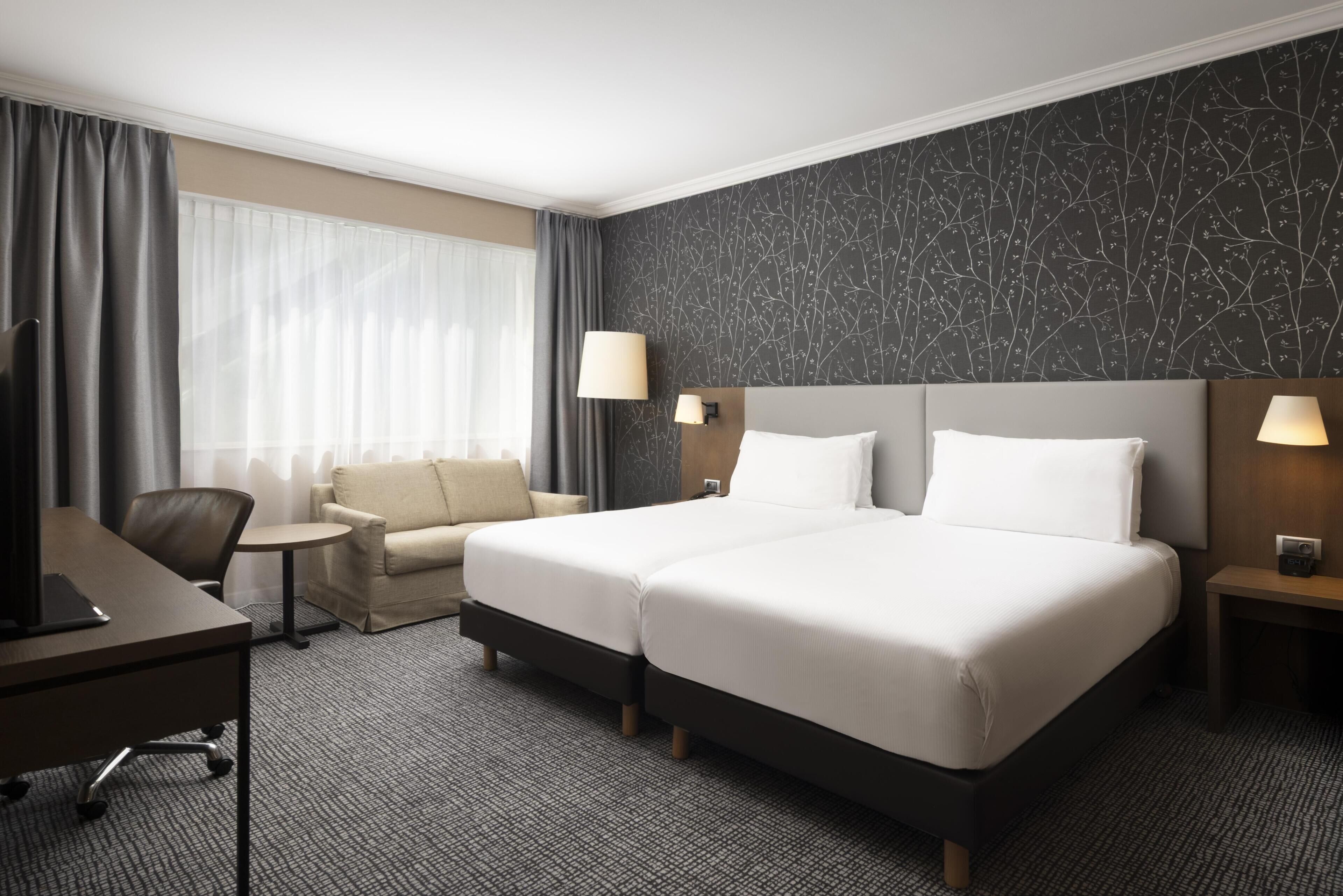 A hotel room with a bed, a desk, a chair, and a small table.