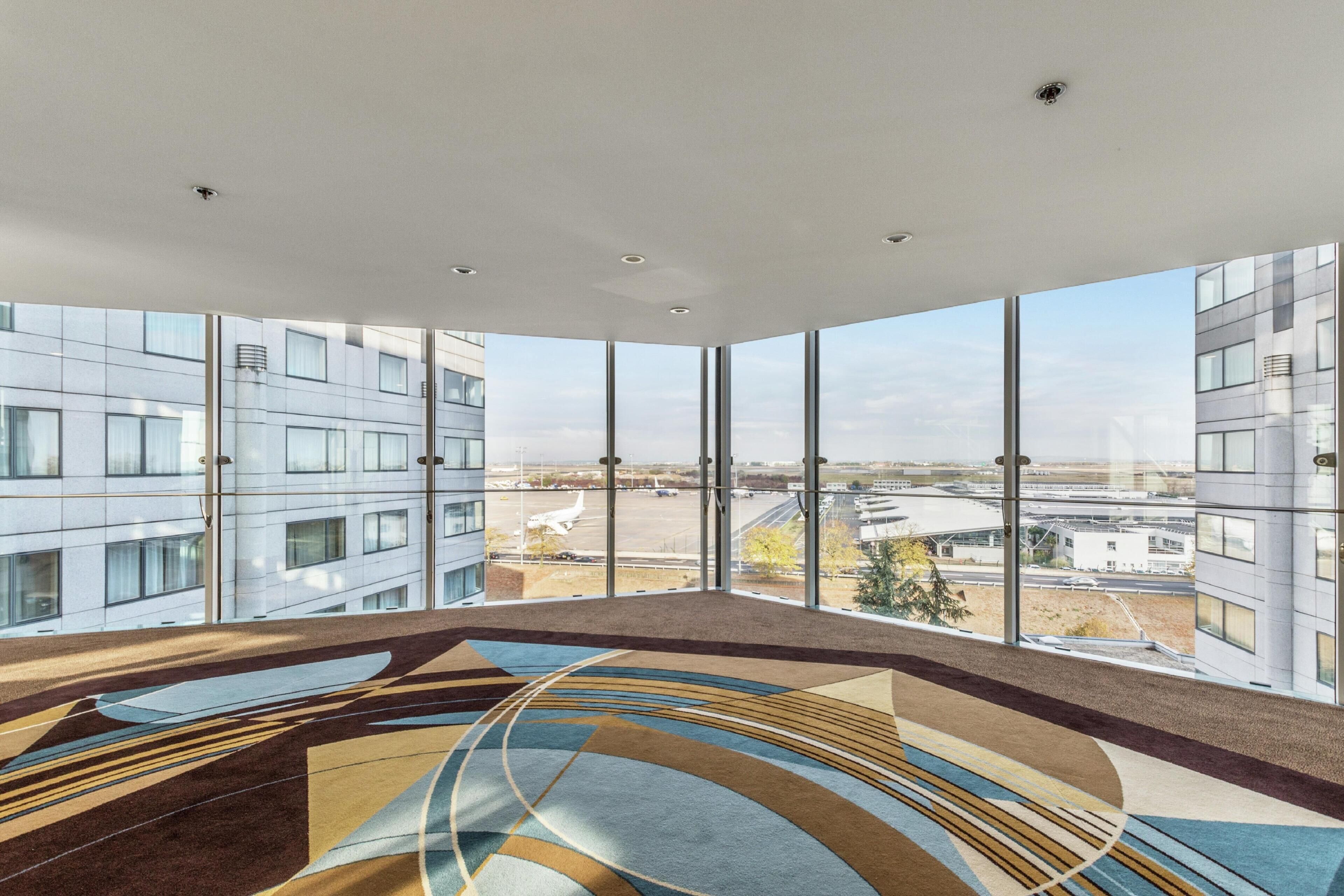 A modern interior with large windows offering a view of an airport and surrounding buildings.