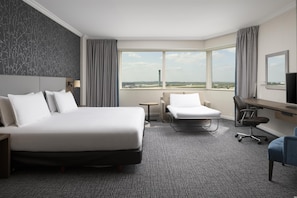 Ein Hotelzimmer mit einem großen Bett, einem Schreibtisch, einem Stuhl und Blick auf das Flughafengelände.