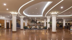 Un lobby amplio con techo curvo, columnas grandes y una zona de estar central con sillas y mesas.