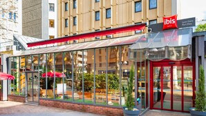 Un restaurant à la façade vitrée, doté d’un auvent rouge, de tables en terrasse et de plantes en pot.
