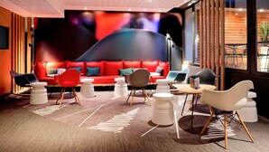 Un espace de détente moderne avec un canapé rouge, plusieurs fauteuils et une grande fresque murale abstraite.