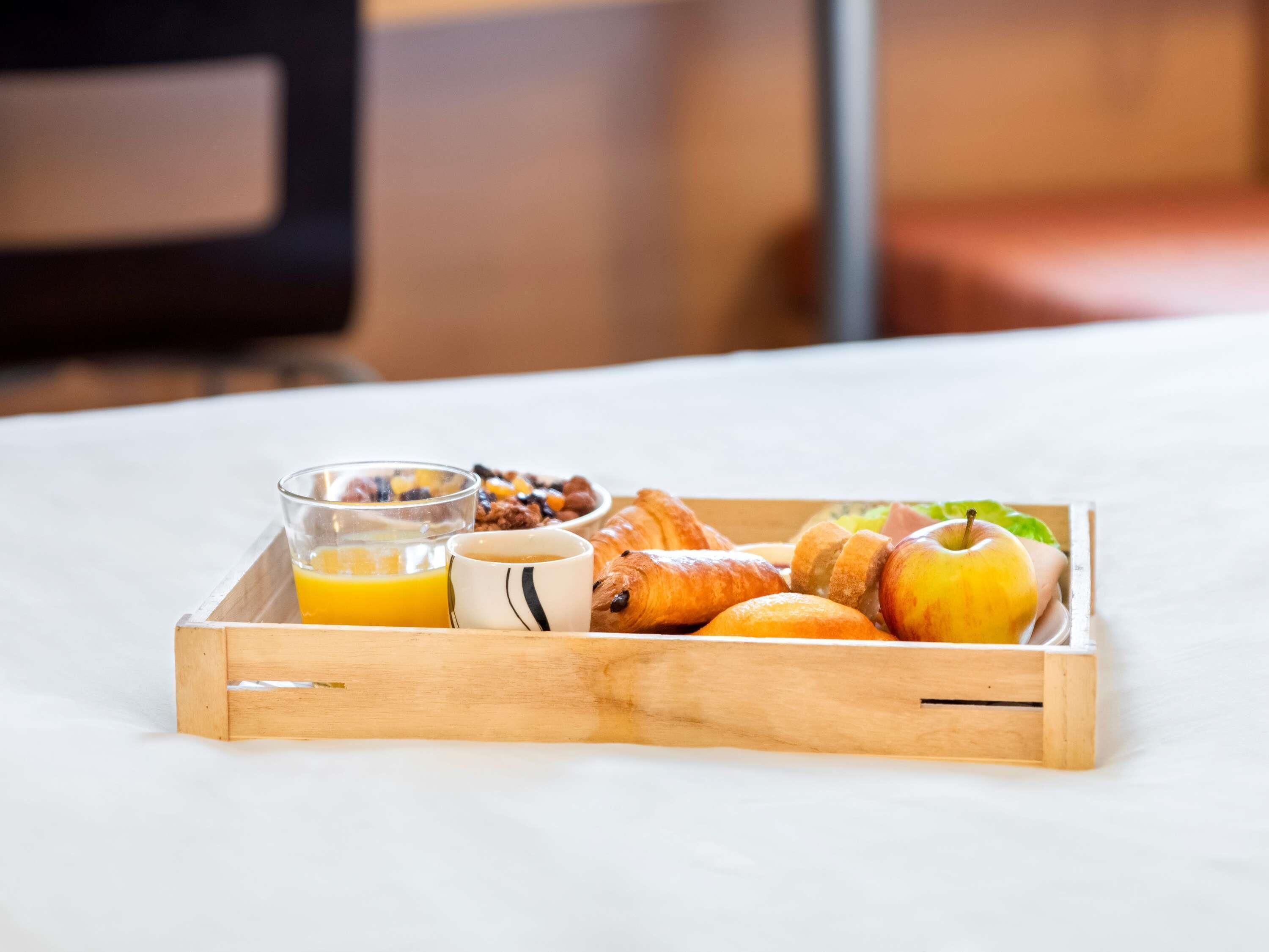 A wooden tray with breakfast items including croissants, an apple, a glass of orange juice, and a mug.