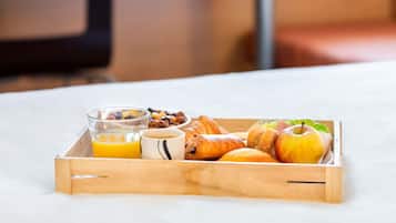 A wooden tray with breakfast items including croissants, an apple, a glass of orange juice, and a mug.