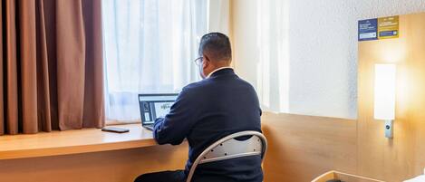 A man sitting at a desk in a hotel room, using a laptop.