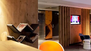 Un espace d’accueil avec un mur en bois, un écran de télévision et un coin salon comprenant une table blanche et une chaise bleue.