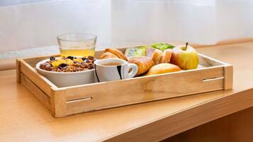 A wooden tray with breakfast items including cereal, a glass of orange juice, a croissant, an apple, and a cup of coffee on a wooden table near a window.