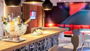 Un coin bar avec un présentoir rempli de bouteilles de champagne, un téléviseur et, au fond, un espace détente avec des sièges rouges.