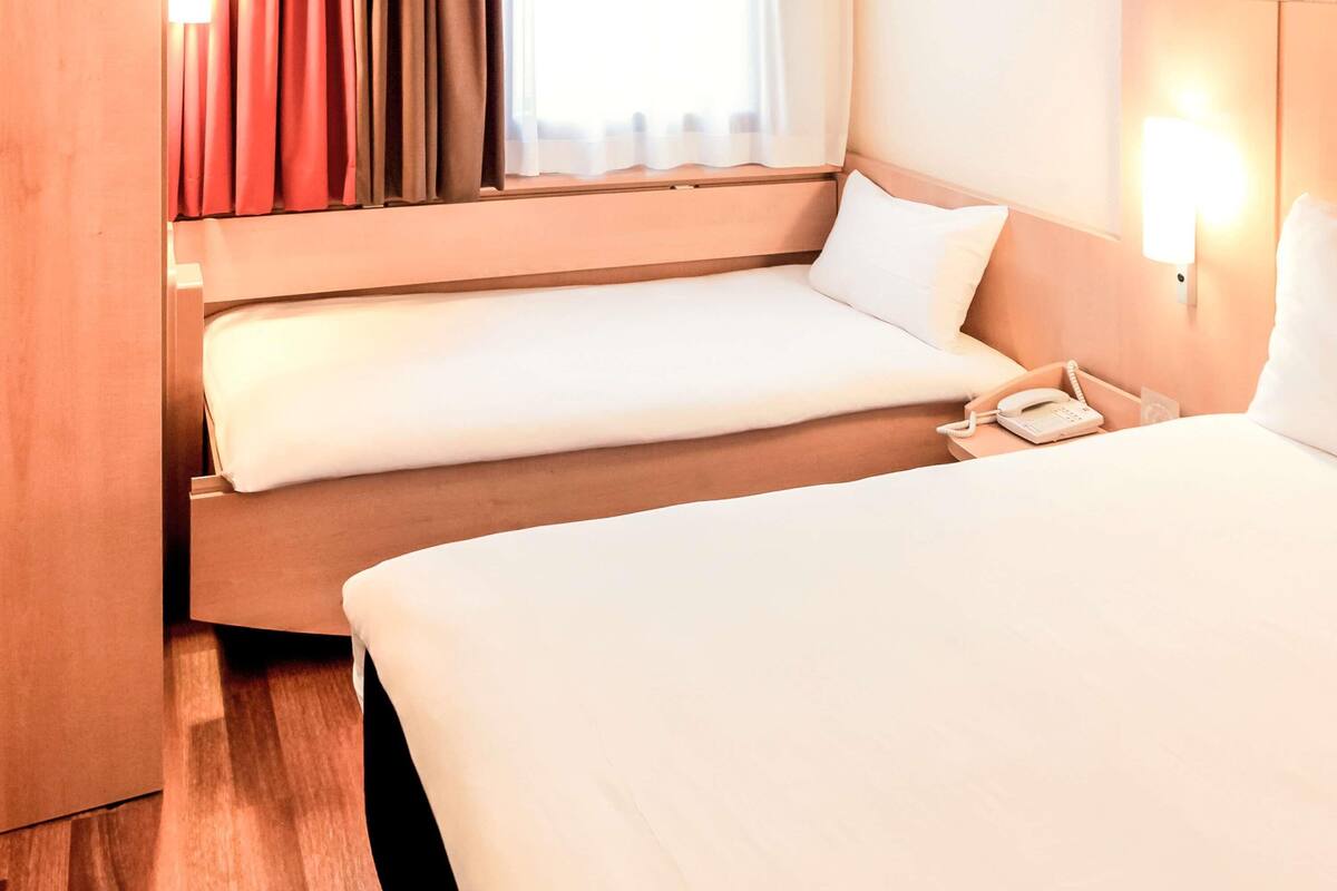 Habitación de hotel con dos camas, teléfono junto a la cama y una ventana con cortinas.