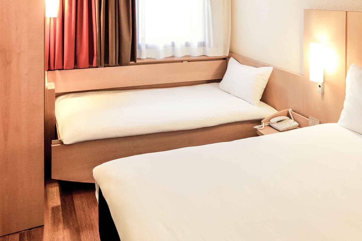 Une chambre d’hôtel avec deux lits, un téléphone sur la table de chevet et une fenêtre avec des rideaux.