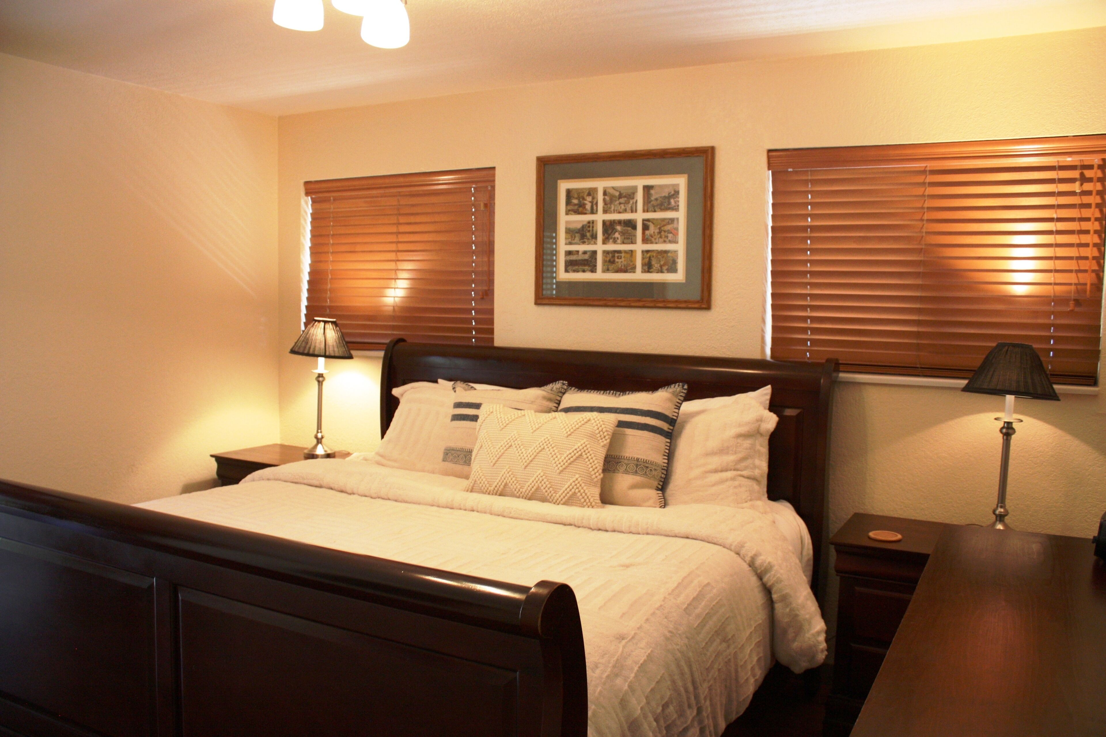 A neatly made bed with a wooden headboard, two bedside tables with lamps, and a framed picture on the wall.