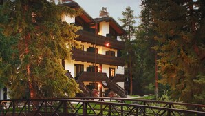 A multi-story building with a wooden staircase leading to a balcony, surrounded by dense forest and a small stream. - Vail Racquet Club Mountain Resort (Vail)