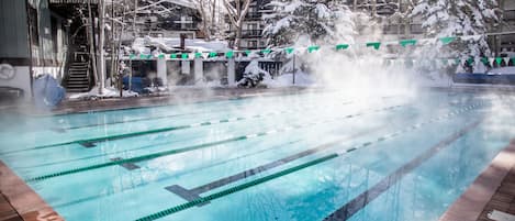 A swimming pool with clear lane dividers, surrounded by buildings and trees covered in snow.