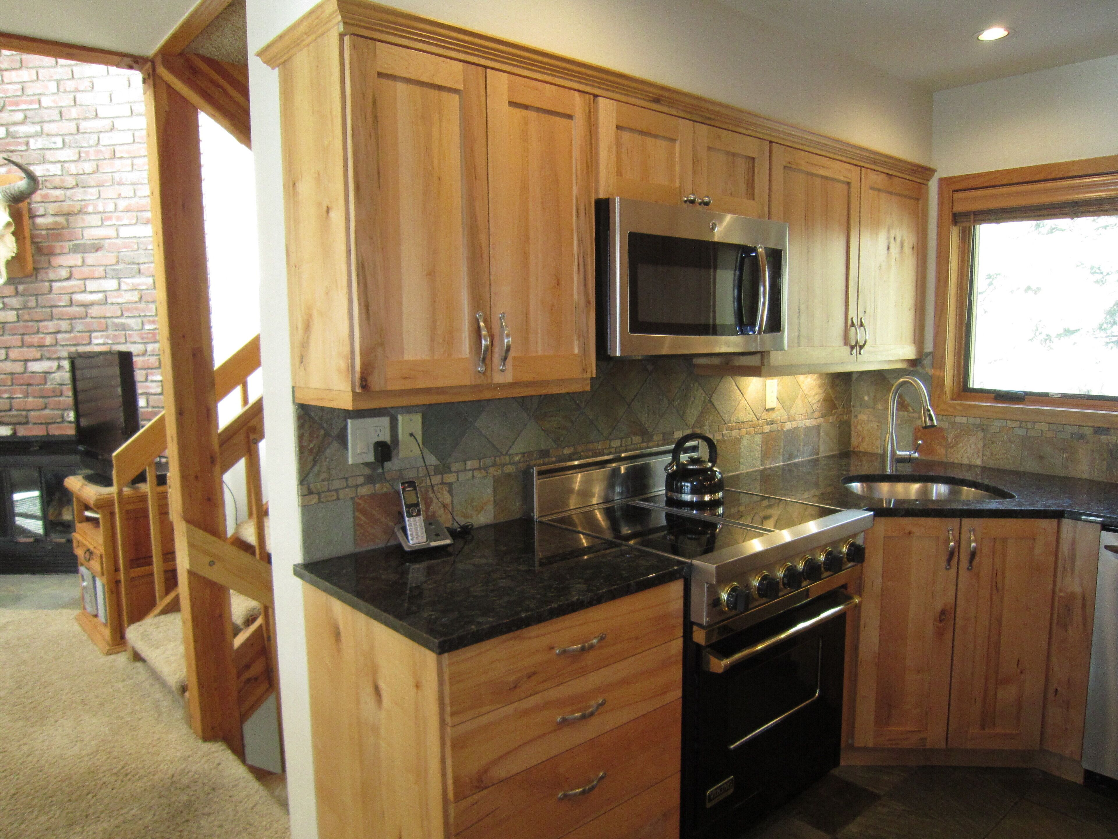 A kitchen with wooden cabinets, a stainless steel microwave, a stove, and a sink.